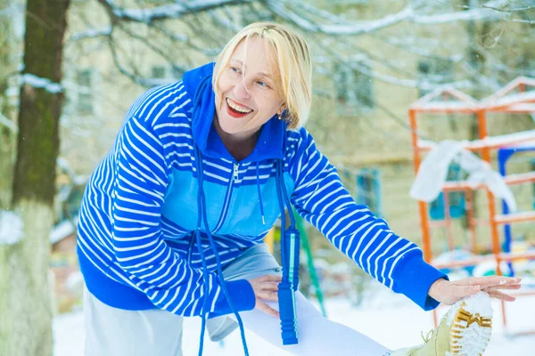 fit active old blond woman performing training and doing her warming up exercise with jumping rope outdoors snowy winter