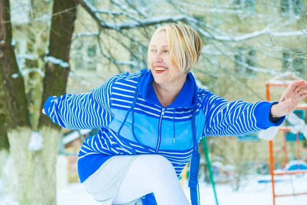 fit active old blond woman performing training and doing her warming up exercise with jumping rope outdoors snowy winter