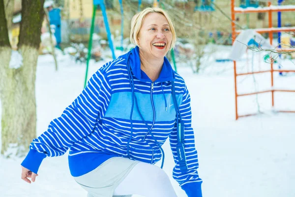fit active old blond woman performing training and doing her warming up exercise with jumping rope outdoors snowy winter