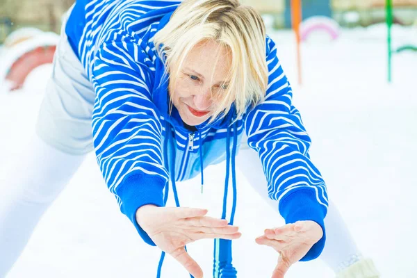 fit active old blond woman performing training and doing her warming up exercise with jumping rope outdoors snowy winter