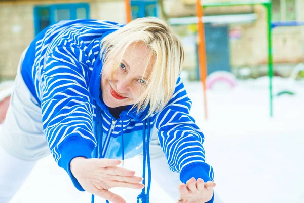 Aktif, sarışın bir kadın antrenman yapıyor ve ısınma egzersizini açık havada, karlı havada ip atlarken yapıyor.