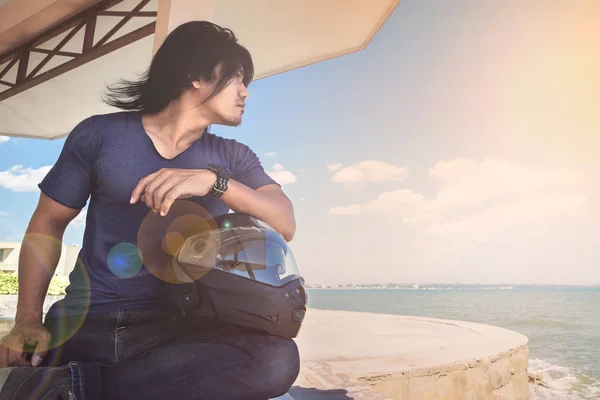 Kaskı ile denize bakarken deniz yanında çatı altında oturan bir Asya adam