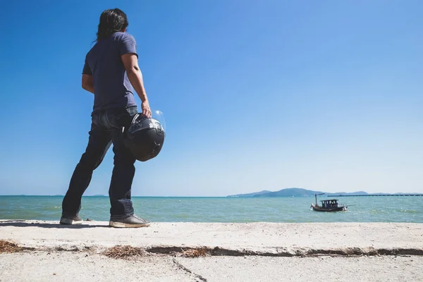 Bir Asya adam stand kaskını tutarak ve tekneye seyir sırasında denizin yanında sırt çevirmek