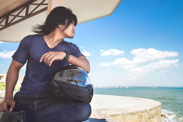 Kaskı ile denizin yanında çatı altında oturan bir Asyalı adam 