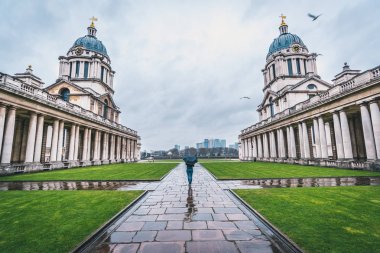 Yağmurlu gün Greenwich Üniversitesi kaldırımda şemsiye ile kadın siluet.
