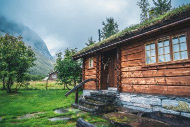 traditional wooden Norwegian cabins in foggy mountains clipart