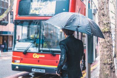 Londra, İngiltere - Mart, 2016: Kırmızı otobüs yağmurlu günde Londra'da bekleyen şemsiye yolcu