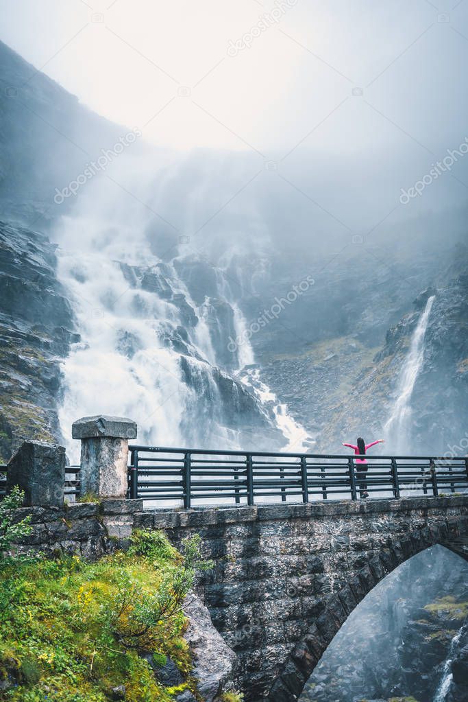woman standing on old bridge with umbrella and enjoying huge waterfall in Norwegian mountains.