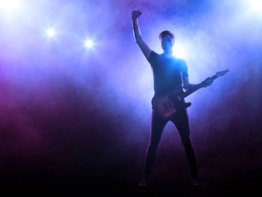 Gitaristin silueti mavi arkaplanda, sahne ışıkları ve dumanla