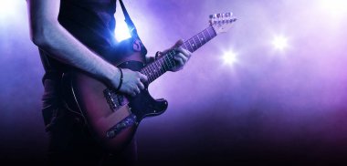 Gitar çalan gitarist. Floodlit arka planı. Kapat.