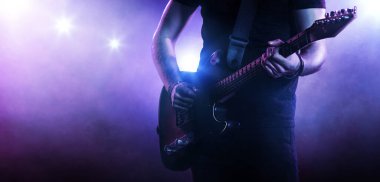 Gitar çalan gitarist. Floodlit arka planı. Kapat.