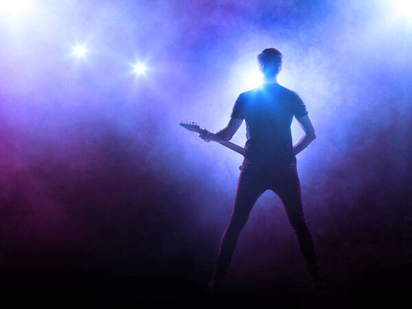 Silhouette of guitar player performing on stage in front of audience.  