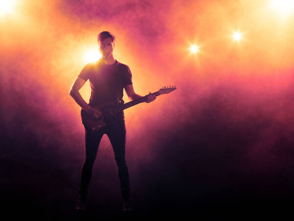 Silhouette of a guitar player on stage. Musical performance. Floodlit background