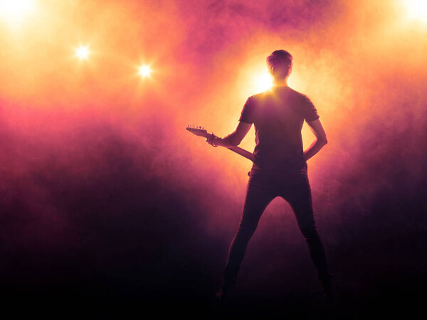 Silhouette of a guitarist performing on stage. Orange smoky background, spotlight