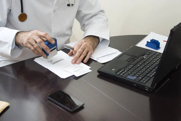  Doktor el reçete üzerinde damgalı. Doktor onun masasında bir reçete yazıyor. 