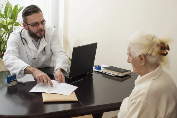Лікар показує пальцем, що пише в історії хвороби пацієнта . — стокове фото