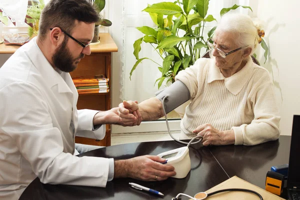 Eine Privatarztpraxis. Der geriatrische Arzt nimmt die Patientin und misst ihren Blutdruck. — Stockfoto