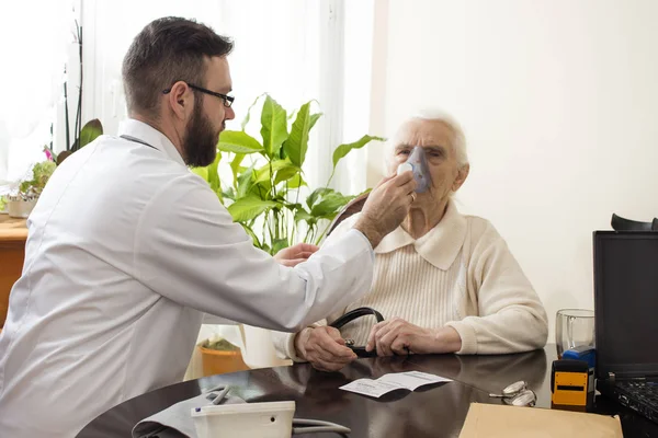 Lääkäri pitää inhalaattoria vanhan naisen kasvoina. . — kuvapankkivalokuva