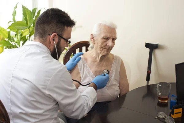 Legen undersøker en gammel kvinne med stetoskop på legekontoret. . – stockfoto