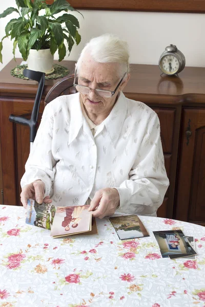 Vieja abuela viendo fotos viejas sentada a la mesa . — Foto de Stock