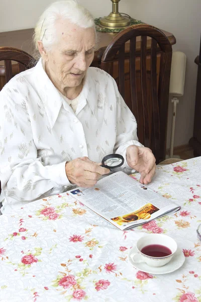 Grandma reads a newspaper article with a magnifying glass. — Stock Photo, Image