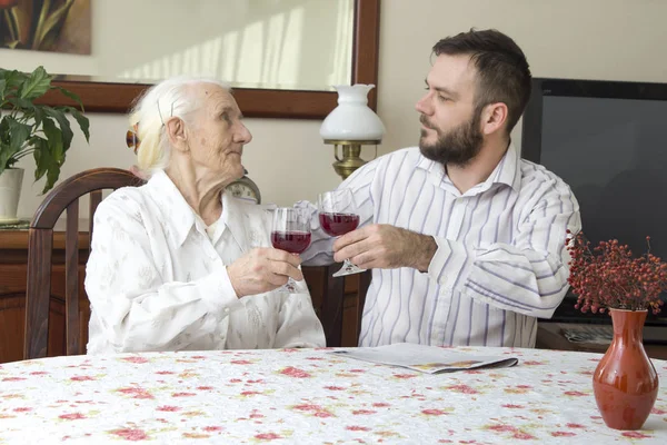 Oma met kleinzoon zitten aan de tafel en toast. Houden van een glas rode wijn. — Stockfoto