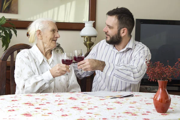 Oma met kleinzoon drinken wijn zittend aan een tafel tijdens een familie bijeenkomst. — Stockfoto