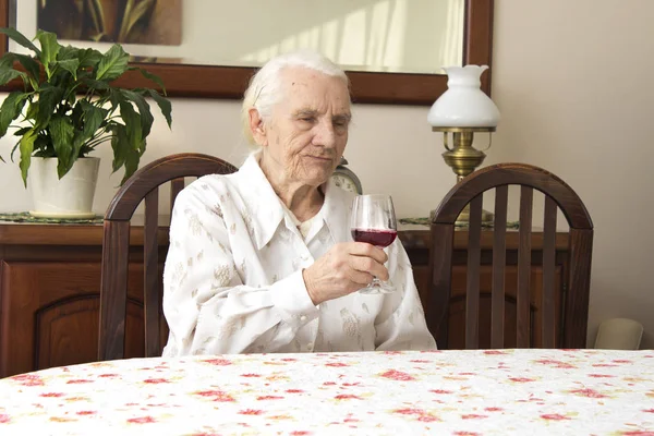 Abuela sentada a la mesa sosteniendo una copa de vino tinto . — Foto de Stock