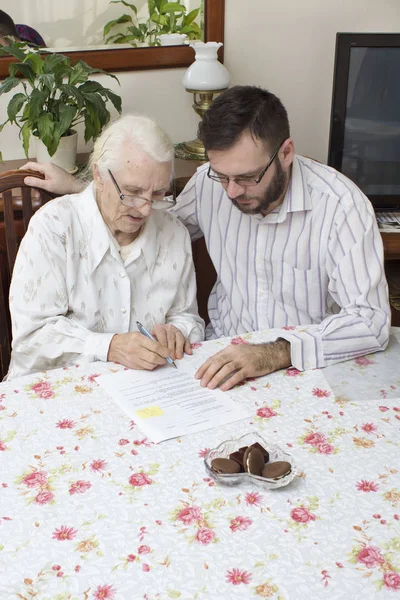 De oude vrouw ondertekent de documenten zitten aan de tafel. — Stockfoto