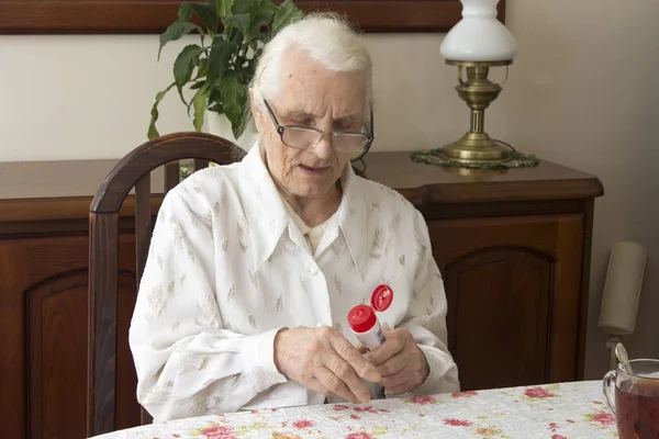 Abuela sentada en una mesa en la sala de estar y lubrica el ungüento de manos . — Foto de Stock