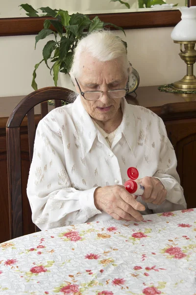 La anciana lubrica la crema de manos sentada a la mesa . — Foto de Stock
