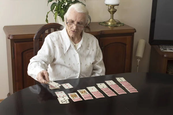 La anciana se sienta en una mesa y pone solitario con cartas — Foto de Stock
