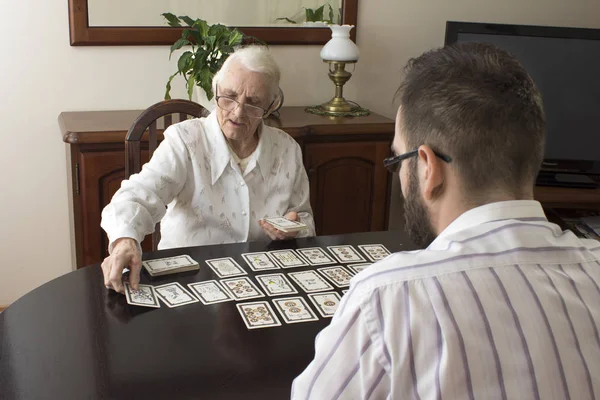 Mujer muy vieja pone un hombre cartas del tarot. La adivinación con cartas del tarot . — Foto de Stock