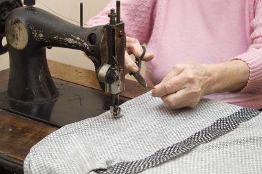 Bir iş parçacığı bir makinede kesme yaşlı bir terzi kadın elinde.