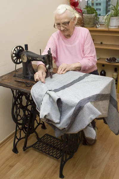 Una vieja mujer de pelo blanco cose en una vieja máquina de coser. Adaptación de una vieja costurera — Foto de Stock