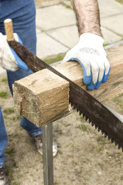 Εργαζόμενος κατασκευή κόβει ένα χέρι είδε σε ένα κομμάτι του ακατέργαστου ξύλου. — Φωτογραφία Αρχείου