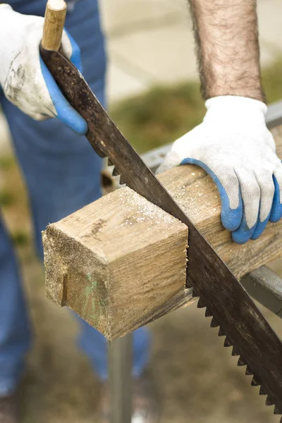 Trabalhador da construção corta uma serra de mão em um pedaço de madeira crua . — Fotografia de Stock