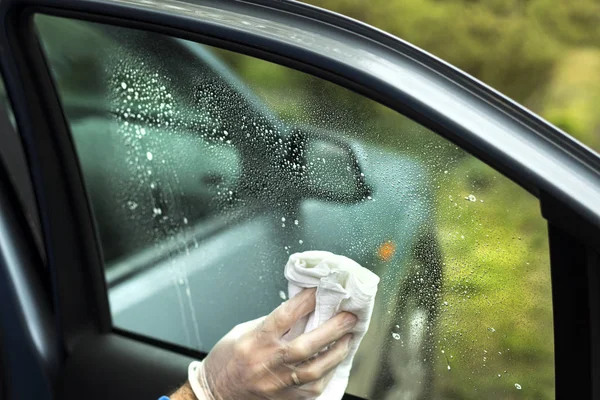 The man\'s hand wipes the car\'s glass with a cloth.