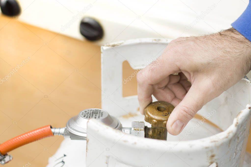 The man's hand unscrews the valve from the gas bottle.