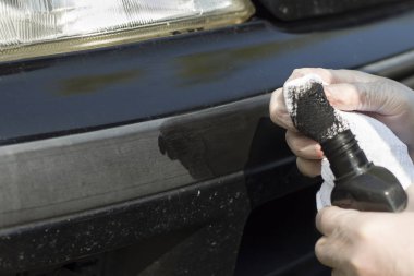 Elini bir hamur siyah yıpranmış plastik tampon araba üzerinde koyar..