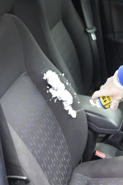 Hand in disposable gloves apply foam to wash the upholstery on the armchair in the car.