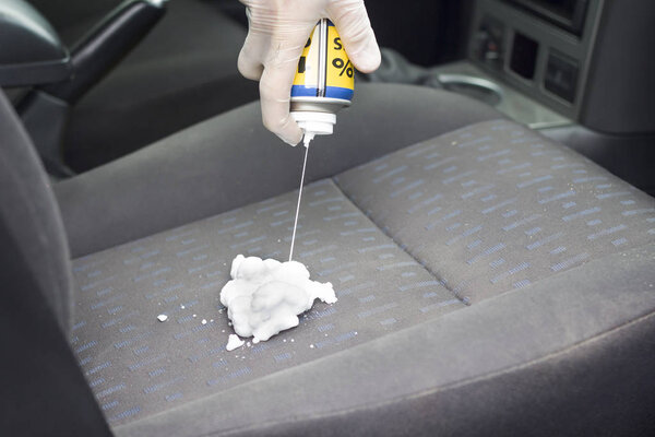 Hand in disposable gloves apply foam to wash the upholstery on the armchair in the car.