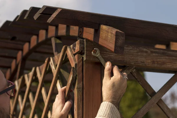 The man\'s hand tightens the screw with a wrench. Renovation and maintenance and repair of wooden garden furniture.