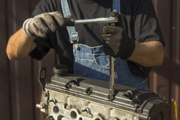 A car mechanic in a work suit unscrews the screws on the engine. Unscrewing the valve cover of the car engine.