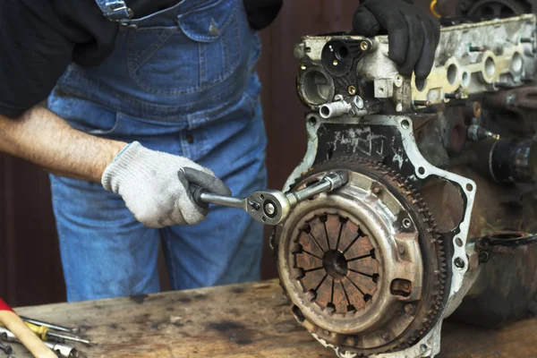 İş eldiveni tamircisi tamirat sırasında motor bloğundaki debriyajı söker..