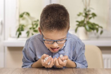 Masada oturan okul çağındaki çocuk. Elinde bir avuç dolusu şeker var. Yanakları şekerle dolu. Dili dışarıdayken, şeker yalamak için uzanır..
