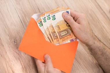 Adamın eli bir zarf tutuyor ve ondan 50 Euro 'luk banknotlarla birlikte Euro banknotlarını çekiyor..