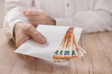 Avro banknotlarıyla dolu beyaz bir zarf tutuyor ve masanın üzerine uzatıyordu..