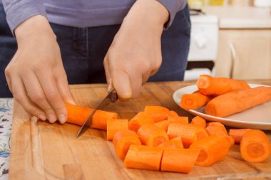 Kadın mutfak tahtasındaki havuçları bıçakla kesiyor..