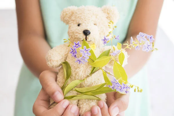 Mano chica sosteniendo osito de peluche jugando y púrpura flores —  Fotos de Stock